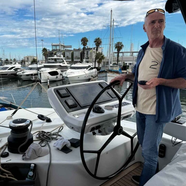 Un capitaine est à la barre d’un Lagoon 82 dans le port de Canet-en-Roussillon, VHF à la main, concentré sur ses manoeuvres de port. Cette scène illustre parfaitement le stress que peuvent générer les manœuvres de port et l’importance de garder un contrôle total de son bateau.